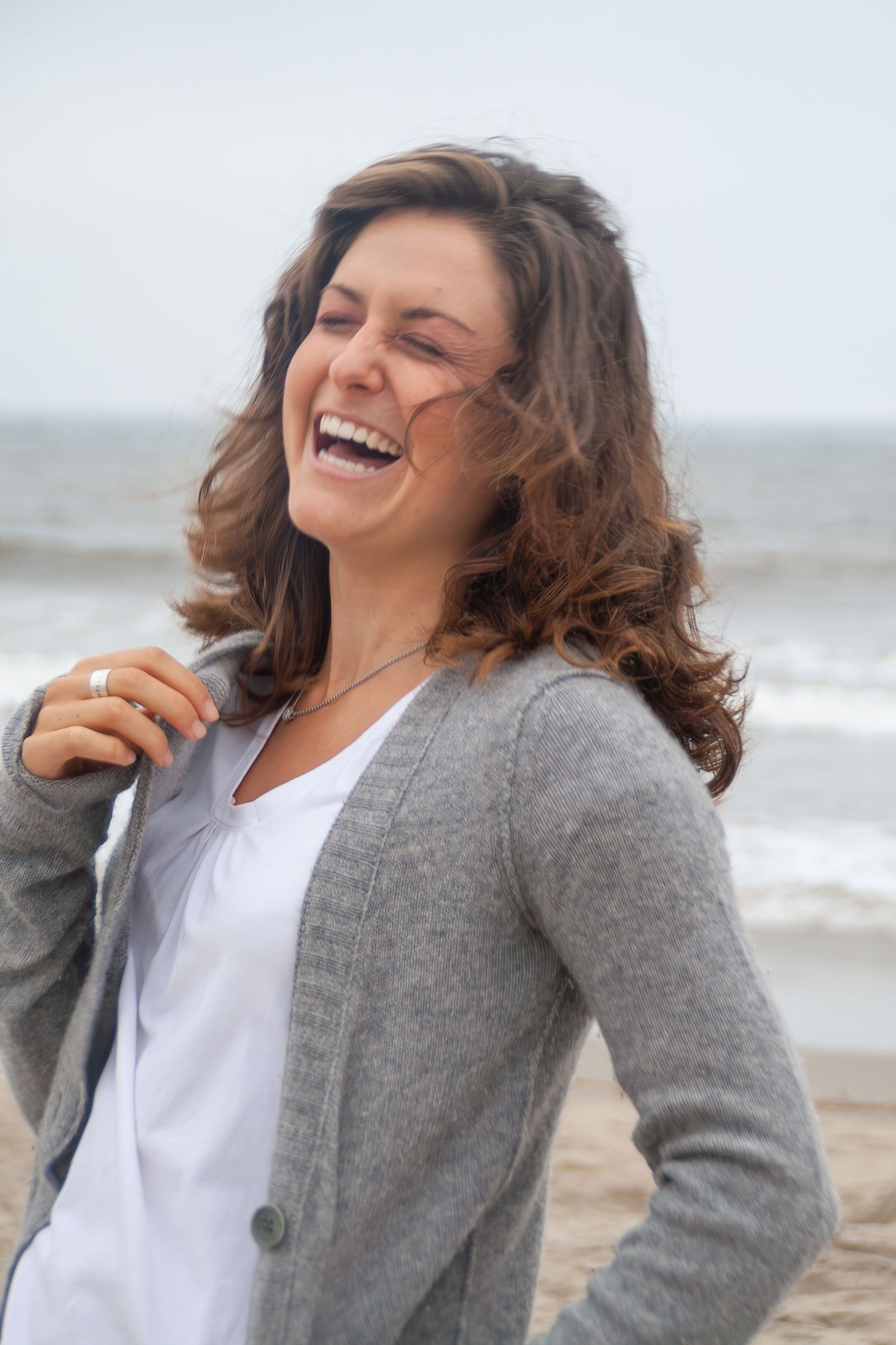 A candid portrait shows joyful laughter at the beach with waves in the background.