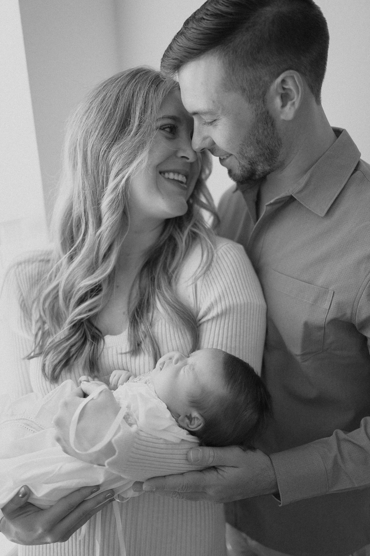 A sweet family moment as parents cradle their newborn baby in a bright minimalist setting.