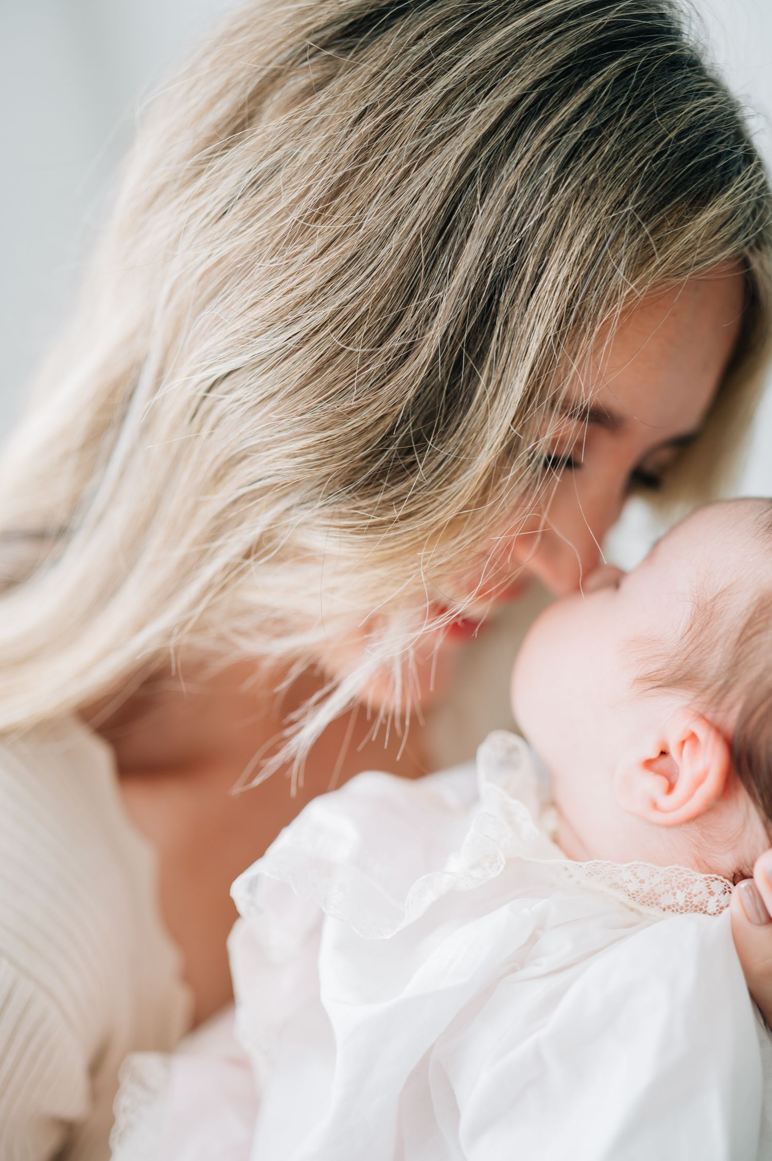 A tender moment between a mother and infant as she leans down to kiss her baby in white.