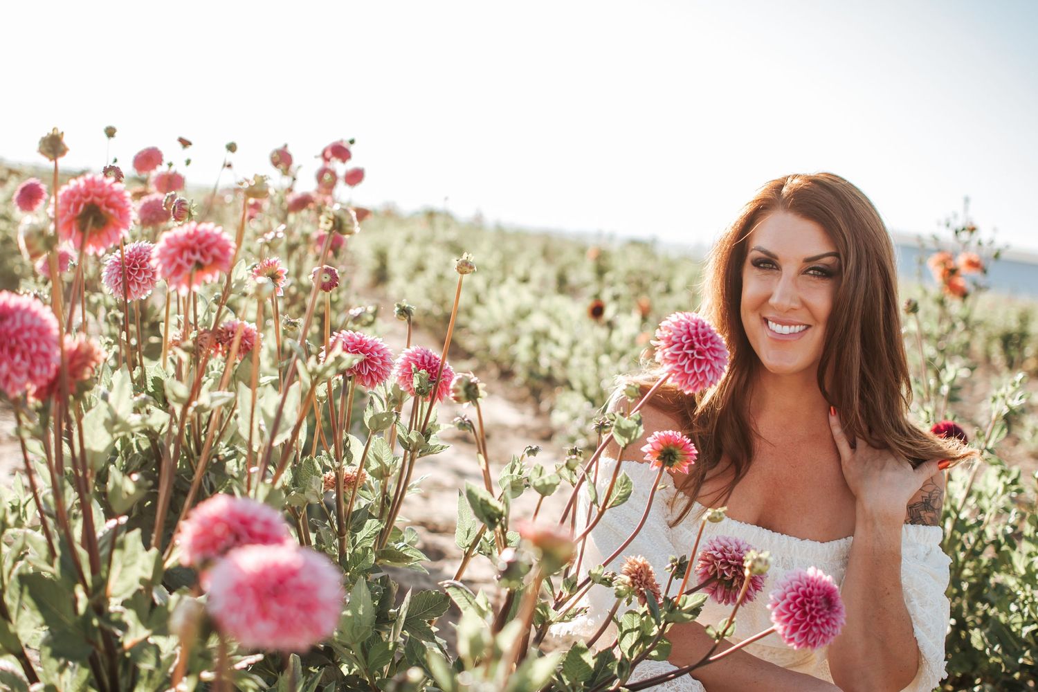 Woman in white dress standing in a vibrant field of pink dahlia flowers on a sunny day in Royal City, Washington at Gray Girl Farms.