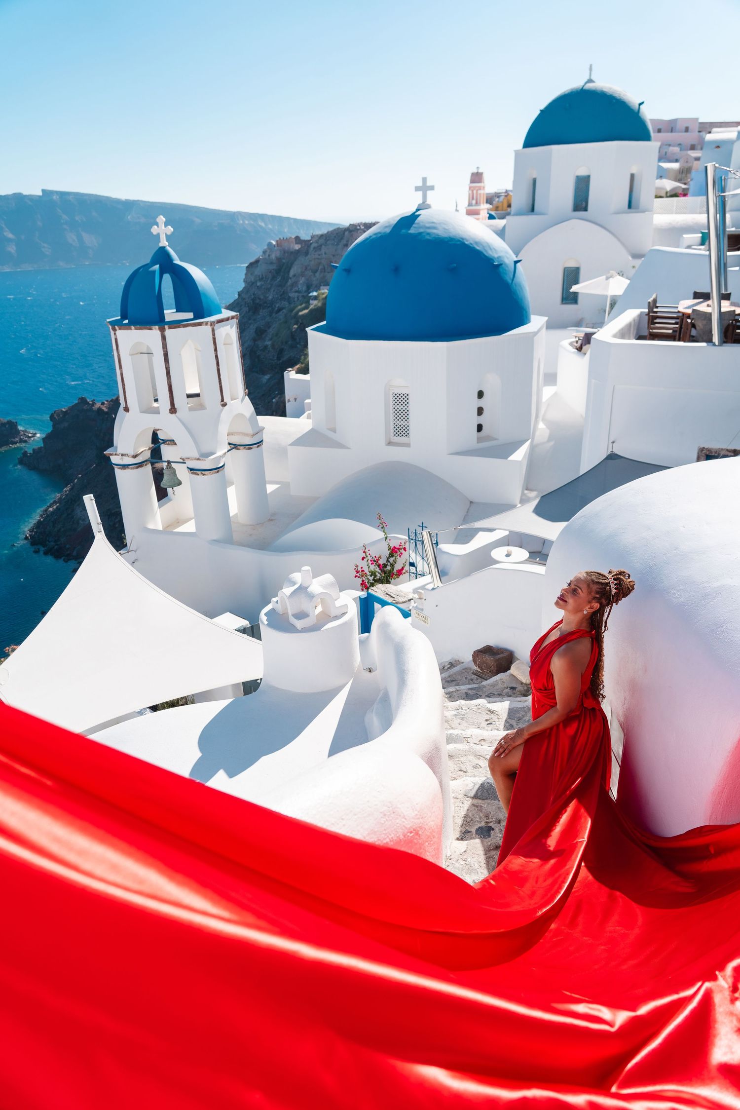 Red flowing dress contrasts with iconic white and blue domed churches in Santorini.