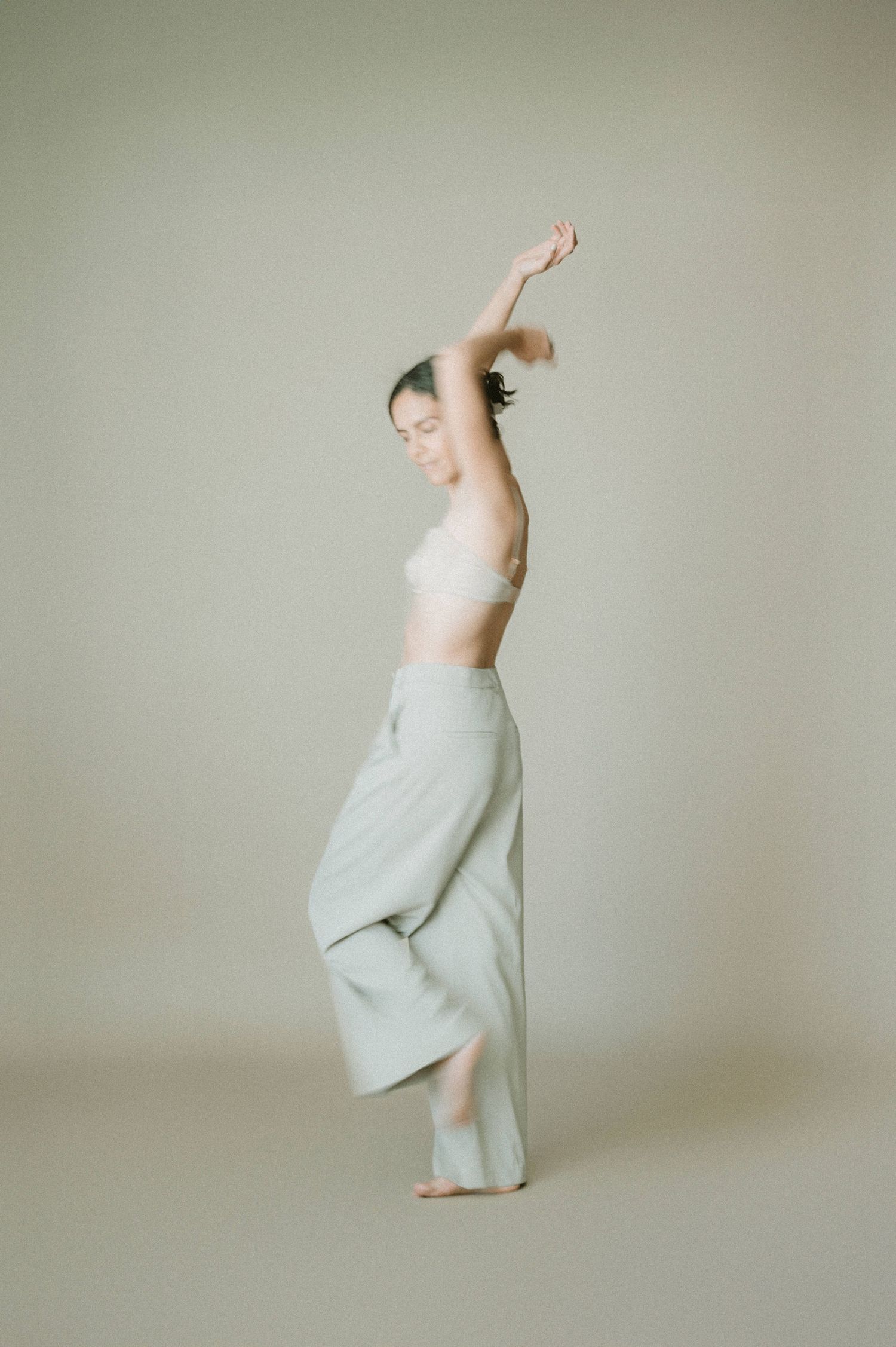Dancer in white performs expressive movement against beige background.