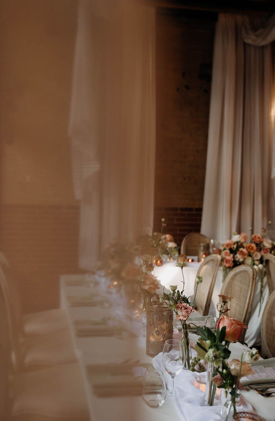 Elegant wedding reception head table adorned with pink and peach floral arrangements, candles, and draped white fabric.