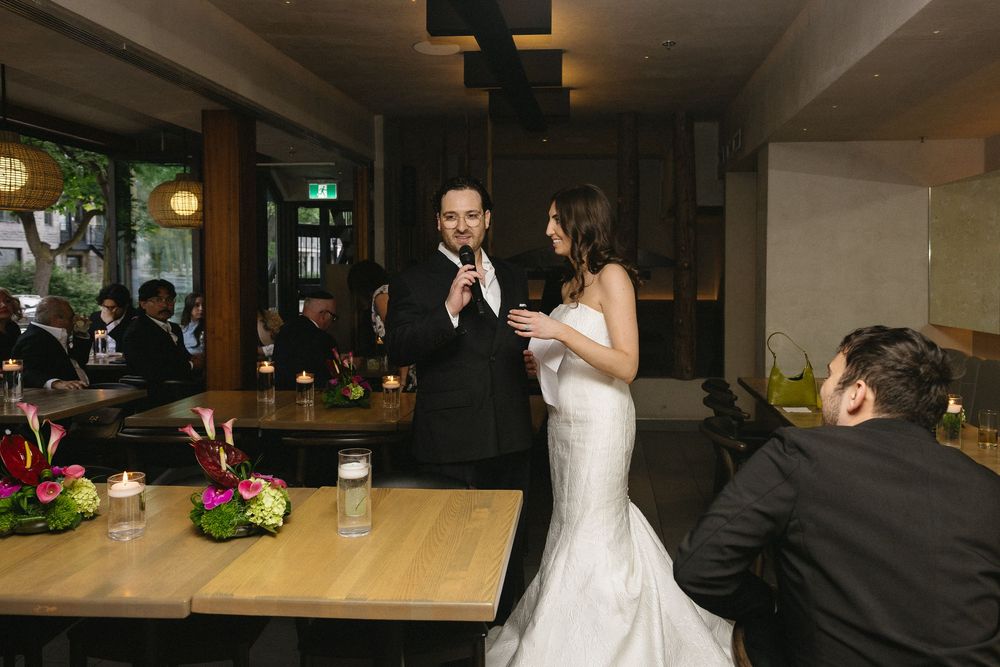 Bride and groom sharing a speech at their elegant indoor wedding reception with floral centerpieces and candlelight.