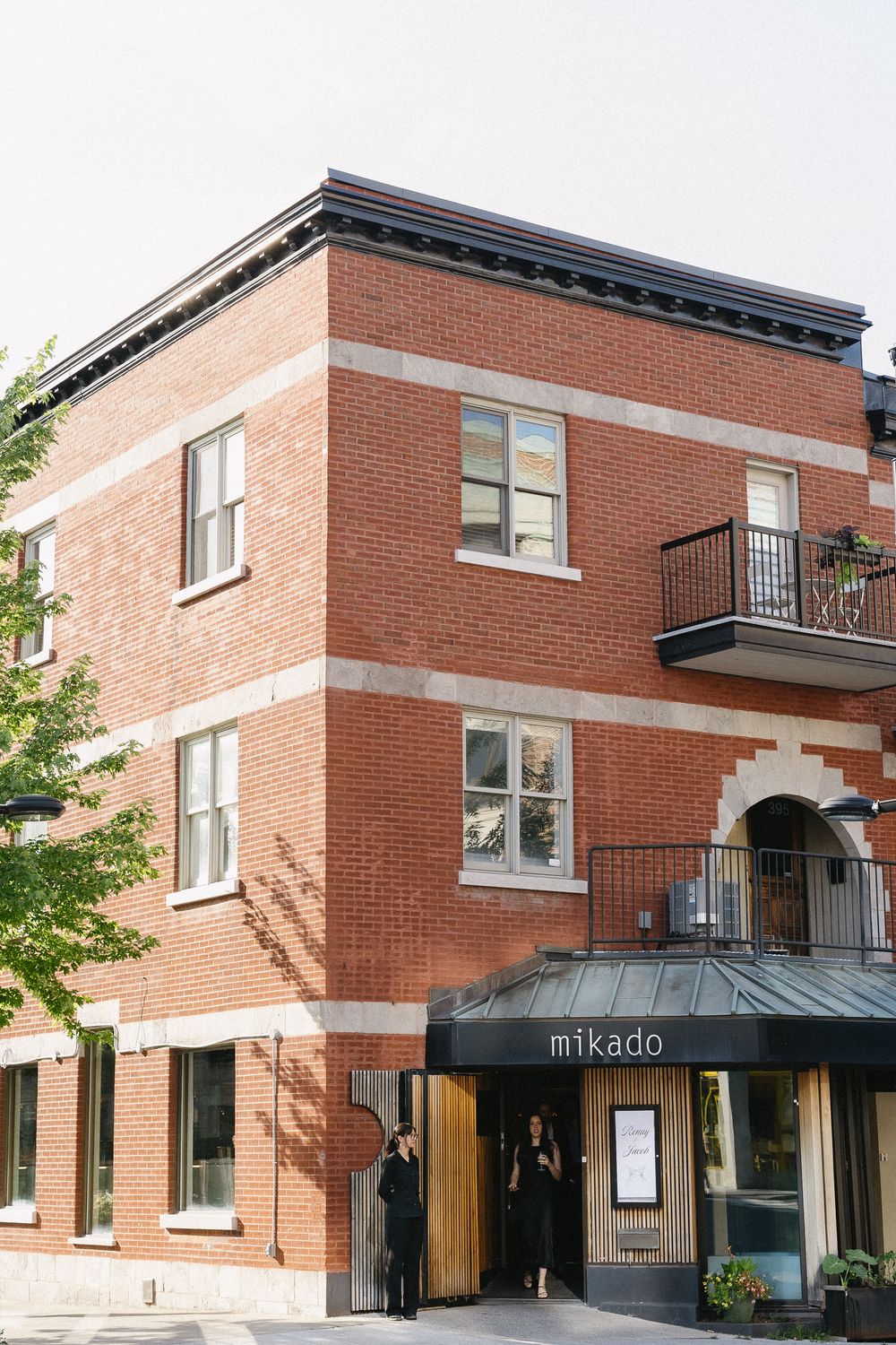 Exterior of Mikado restaurant in a red brick building with black awning and two stories.