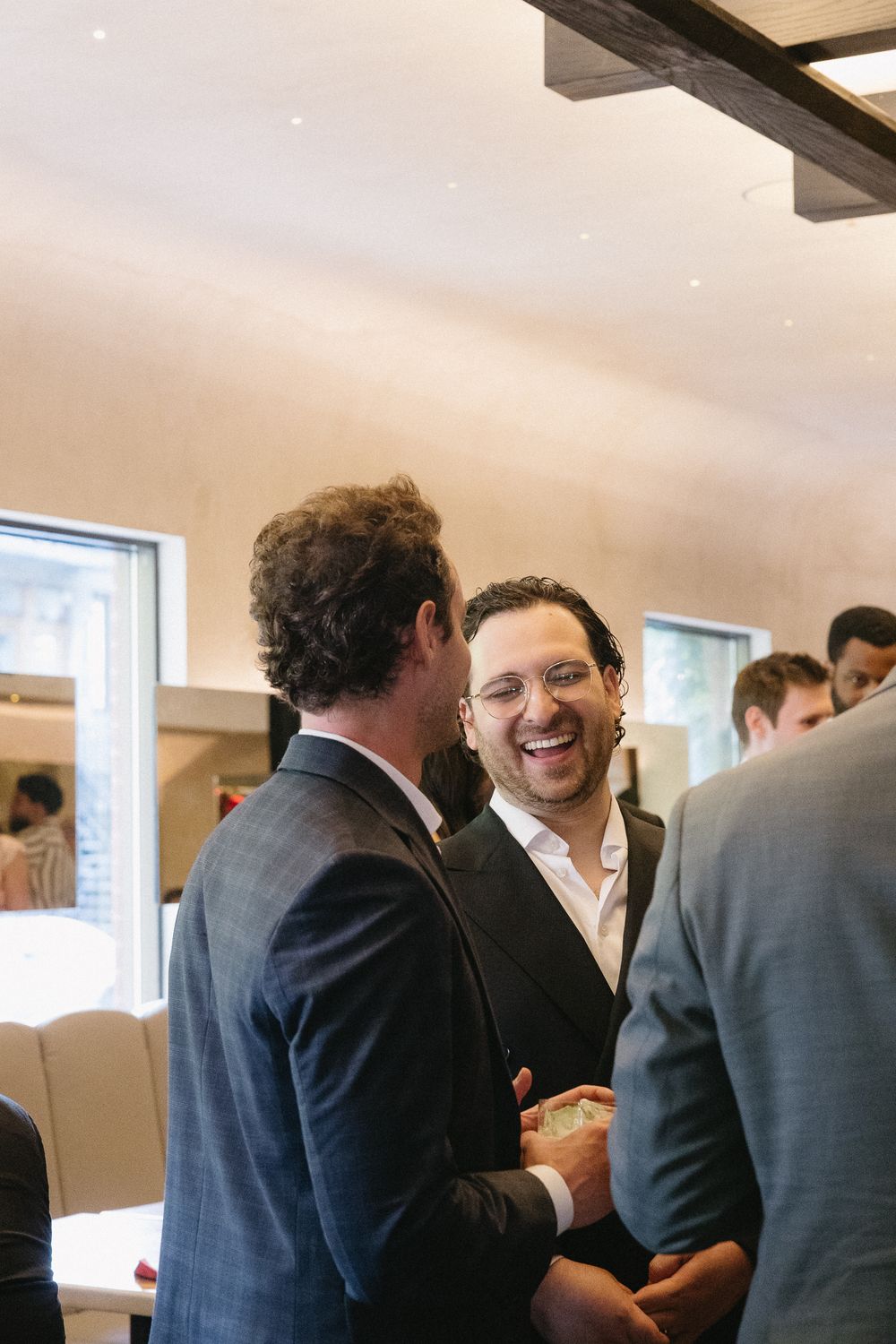 Men in suits laughing and networking at an indoor social event or business gathering.