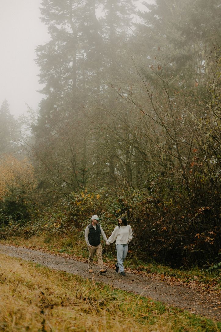 Two people walk along a misty forest path surrounded by autumn foliage on a foggy day.