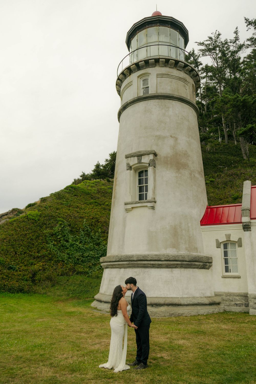 Couple shares a romantic kiss in front of a white lighthouse on the Oregon coast on their wedding day.