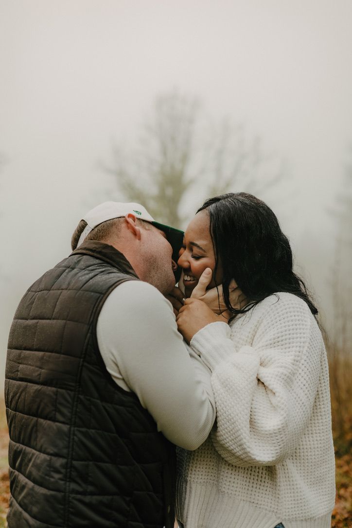 A romantic couple shares tender moments in a misty outdoor setting while wearing cozy winter clothing.