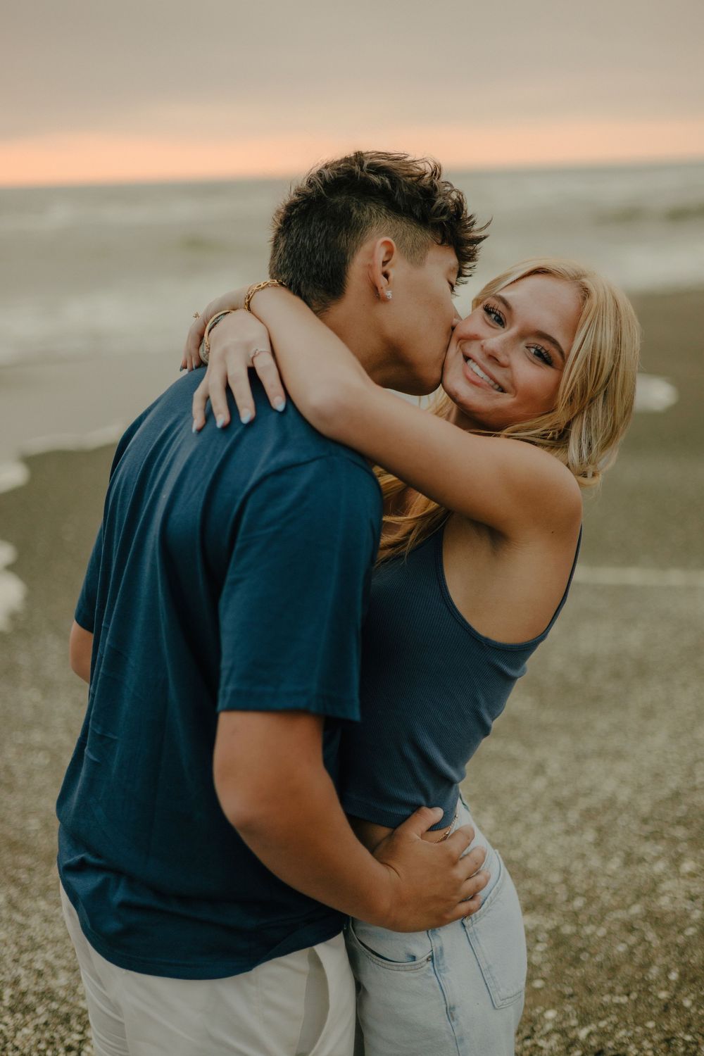 A couple embraces on the beach at sunset, sharing an intimate moment against a warm golden sky.