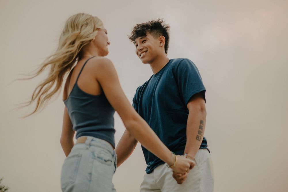 A couple embraces while dancing together in casual attire against a light neutral background.
