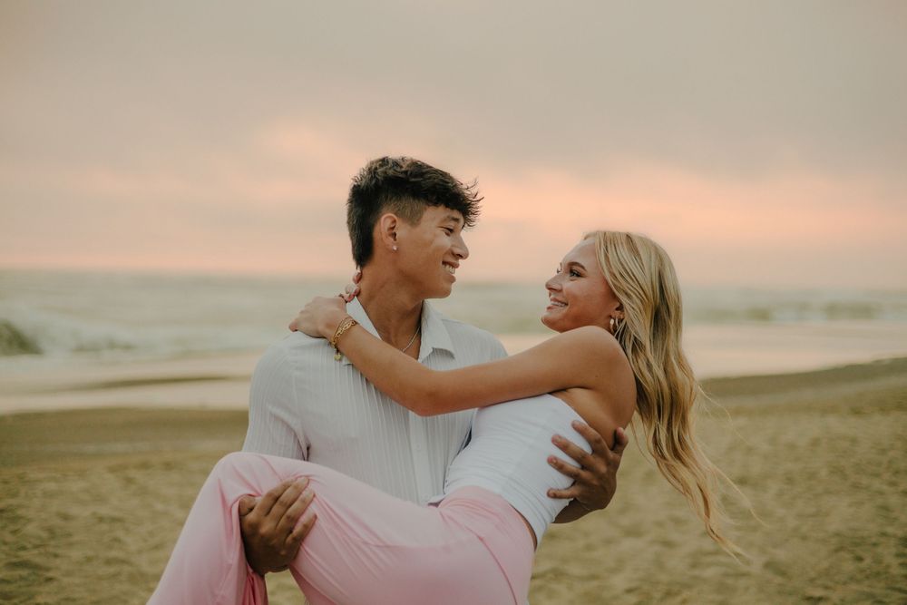 A couple embraces lovingly on a beach at sunset during a romantic photoshoot session.