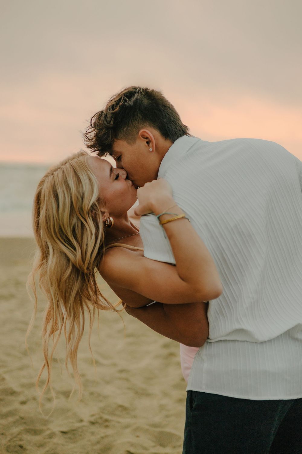 Romantic couple embraces in an intimate moment on the beach at sunset with soft golden lighting.