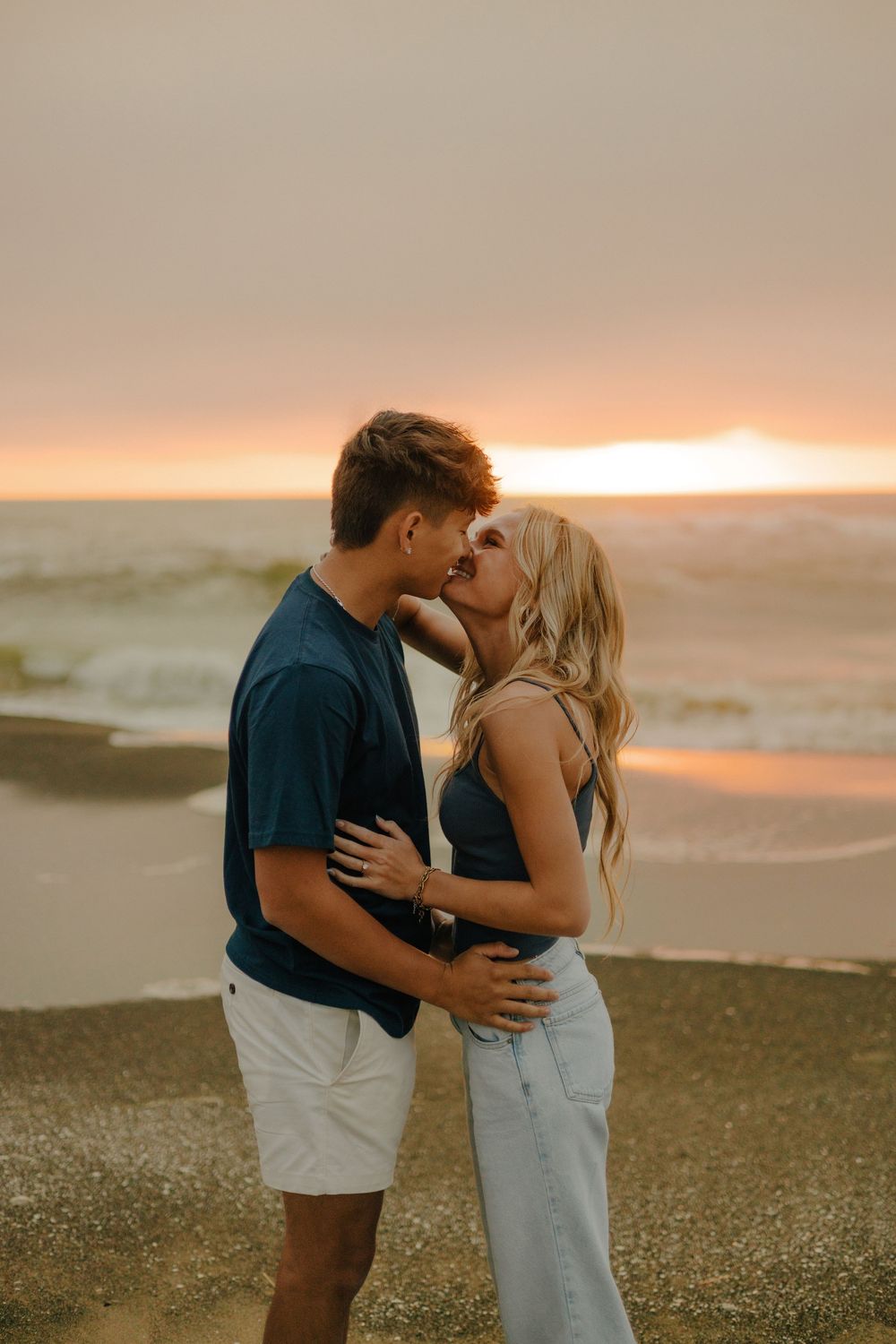 A romantic couple embraces on a beach at sunset with warm golden light illuminating the shoreline.