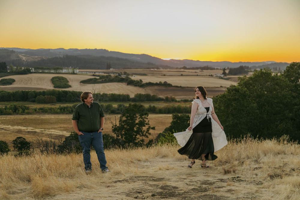 Couple enjoying a golden sunset over rolling vineyards and hills in a scenic countryside landscape.