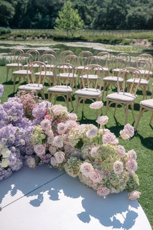 Elegant outdoor wedding ceremony setup with wooden chairs and lush floral arrangements in pink and purple hues.
