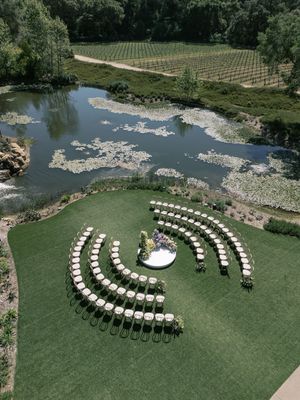Aerial views of white chairs arranged in a curved formation for an outdoor wedding ceremony on a lush green lawn.
