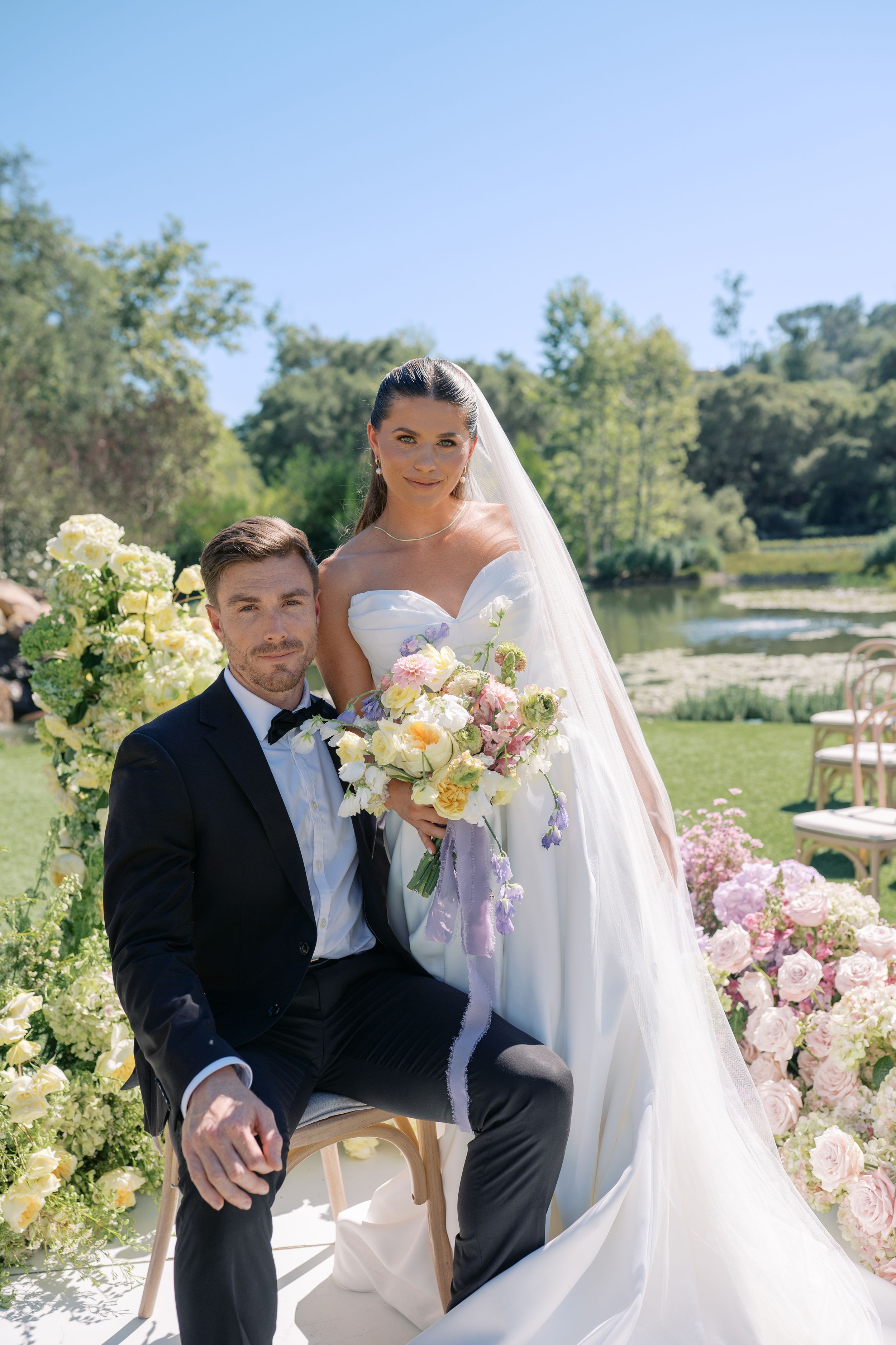 A romantic outdoor wedding photoshoot with a couple posing together in a natural garden setting with pink flowers.