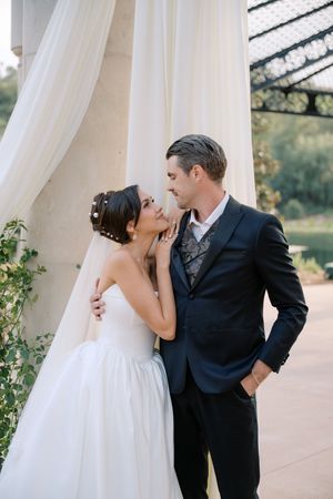 Bride and groom share an intimate moment under white draping at an elegant outdoor wedding venue.