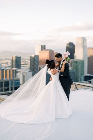 Couple shares romantic moment on a rooftop with dramatic cityscape backdrop at sunset.