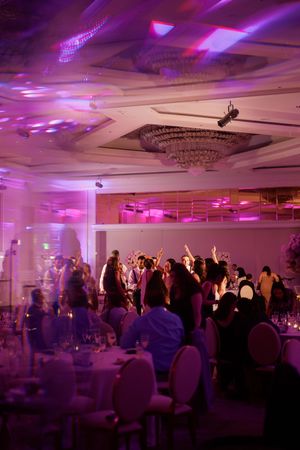 Wedding reception dance floor glows with purple uplighting as guests celebrate under chandelier.