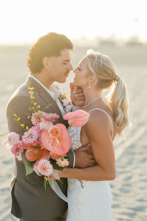 Romantic beach wedding portrait with coral and pink bouquet at sunset.