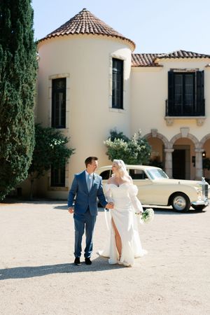 A couple shares a romantic moment in front of a Mediterranean-style villa with terracotta roof tiles and cream walls.