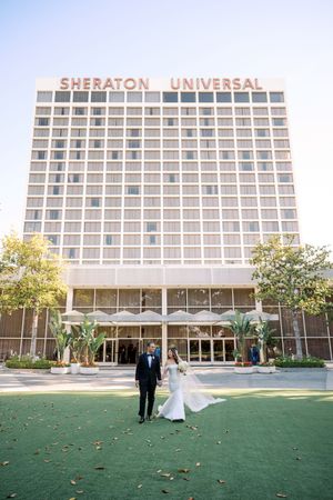 Bride and groom stand on green lawn in front of the Sheraton Universal hotel on their wedding day.