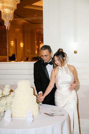 Bride and groom cut three-tier white wedding cake at elegant reception venue.