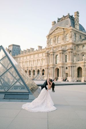 Bride and groom share a romantic dip kiss in front of the Louvre Pyramid in Paris, France.