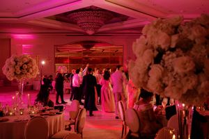Wedding reception dance floor glowing in pink light with floral centerpieces and guests dancing.