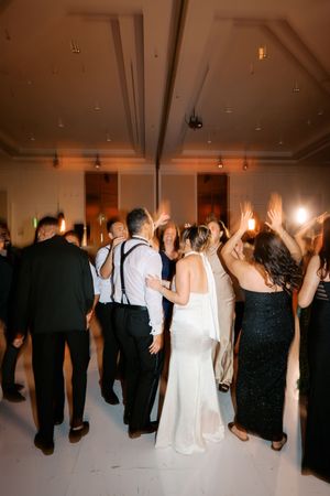 Bride in white halter gown dances with guests on white dance floor at wedding reception.