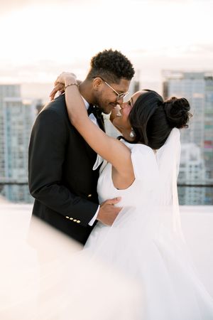 A romantic wedding moment shared between a couple on a rooftop overlooking a cityscape at sunset.