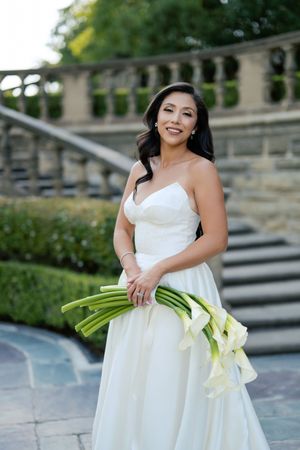 A bridal portrait featuring an elegant white dress and calla lily bouquet on stone steps.
