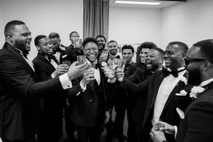 A black and white photo of a celebratory group raising their glasses in formal attire at a special event.