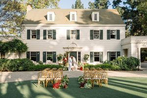 An elegant white colonial house with black shutters set up for an outdoor wedding ceremony.