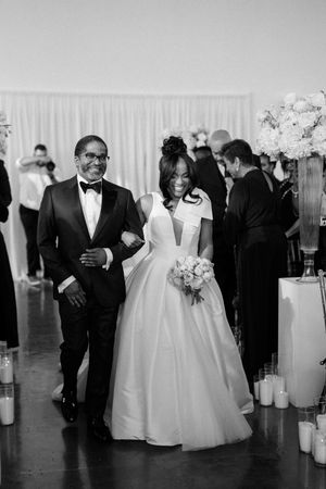 A formal wedding ceremony with a couple walking down the aisle decorated with glowing candles and floral arrangements.