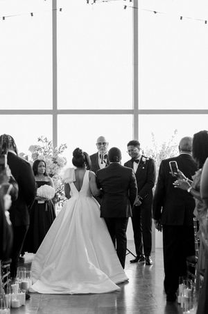 Black and white wedding ceremony photo showing couple at altar during indoor ceremony with guests looking on.