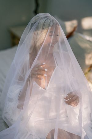 A bride wearing a delicate white veil in soft natural light creates an ethereal and romantic bridal portrait.