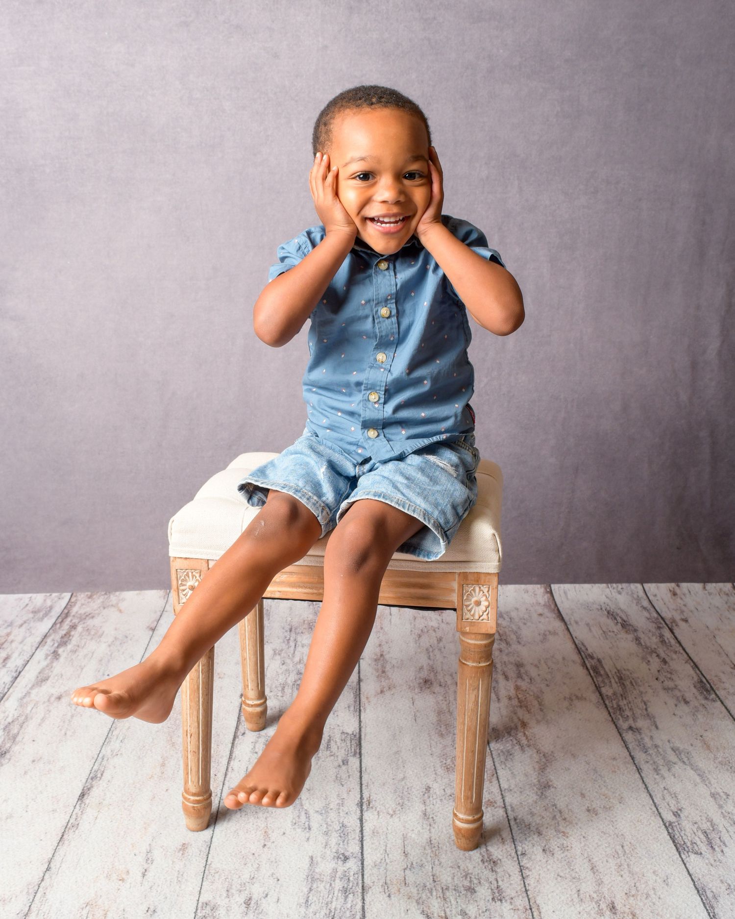 Closeup series of small feet in denim sitting on wooden stool against grey background.