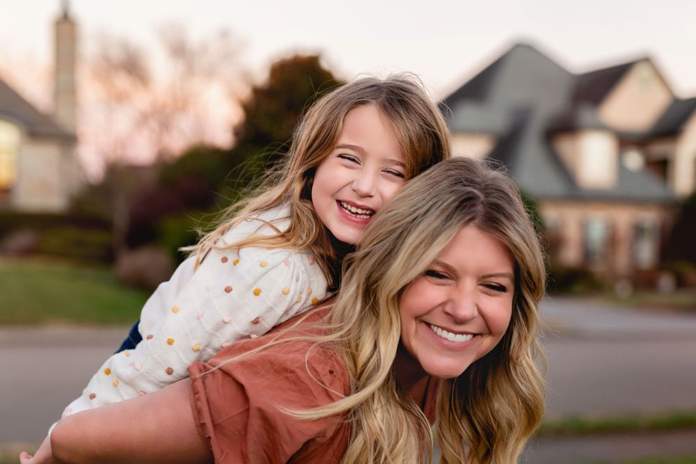 Joyful outdoor piggyback ride in front of residential homes at dusk.
family photography
