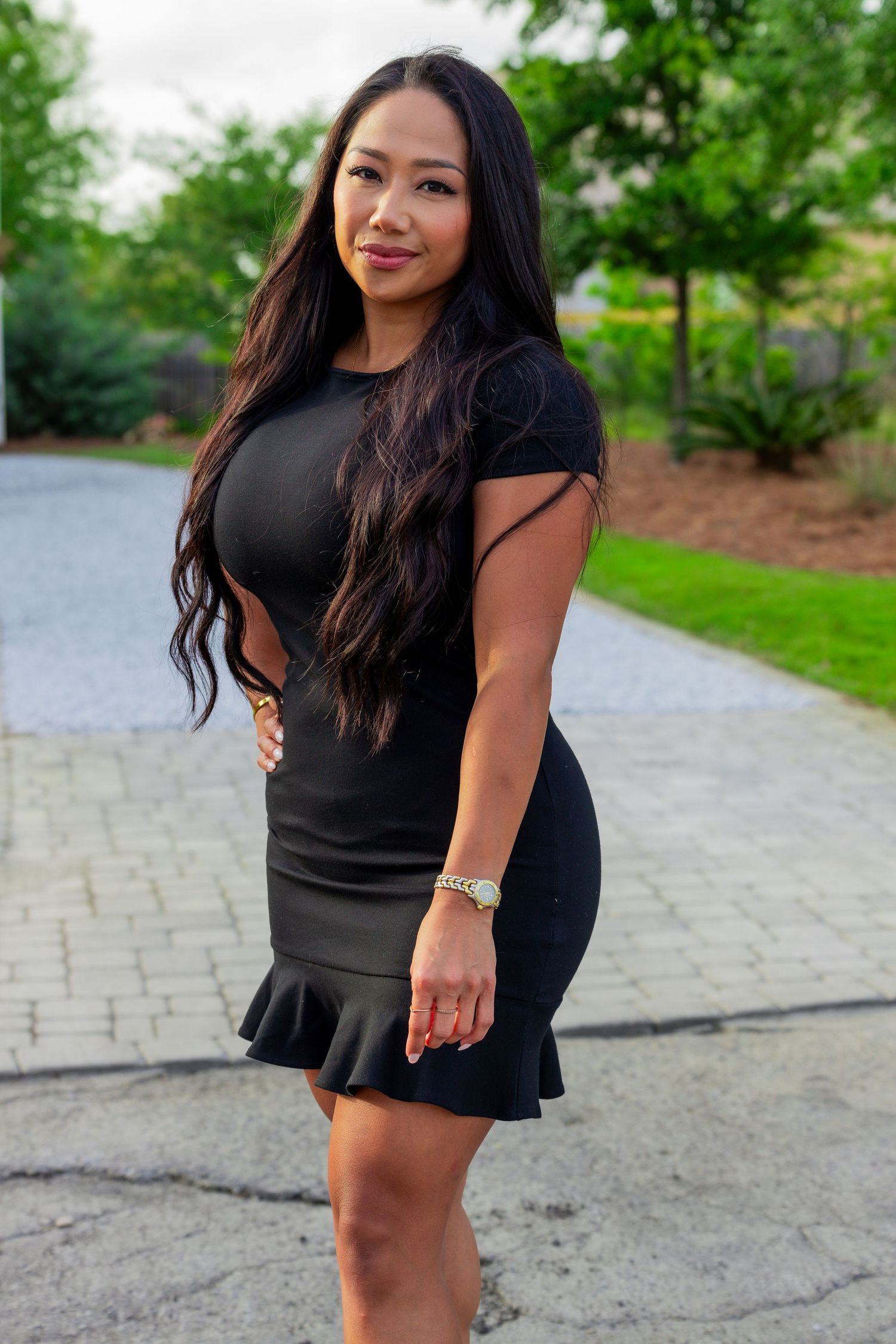A black dress with ruffle hem creates an elegant silhouette against a garden path background.