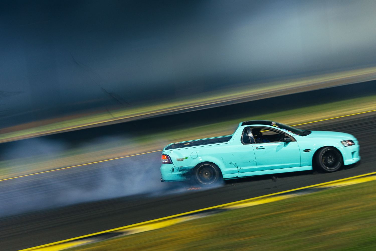 Mint colored sports car drifting on a dark road with motion blur.