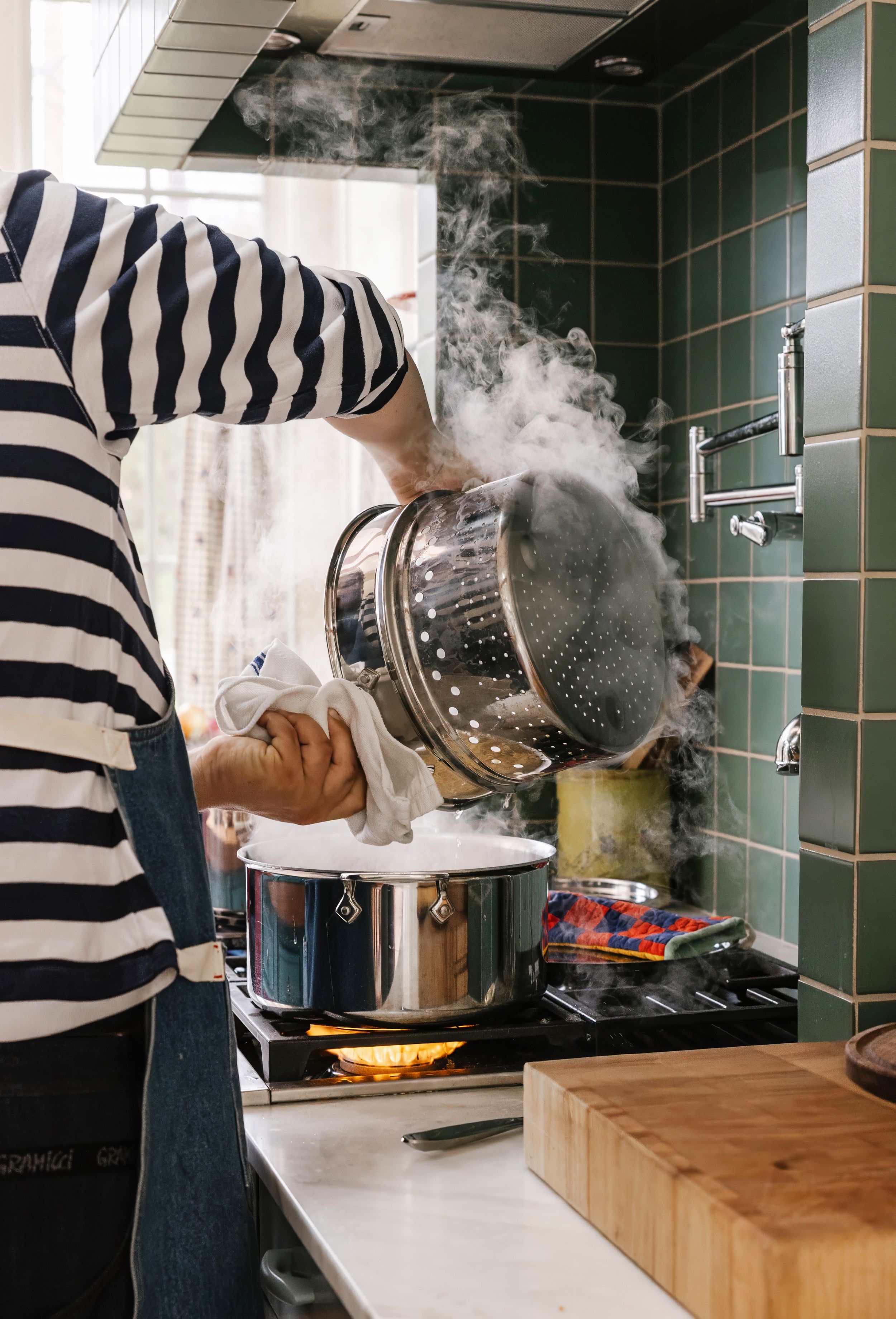 Dan Pelosi lifting steamer basket over a pot on a stove in a green-tiled kitchen.