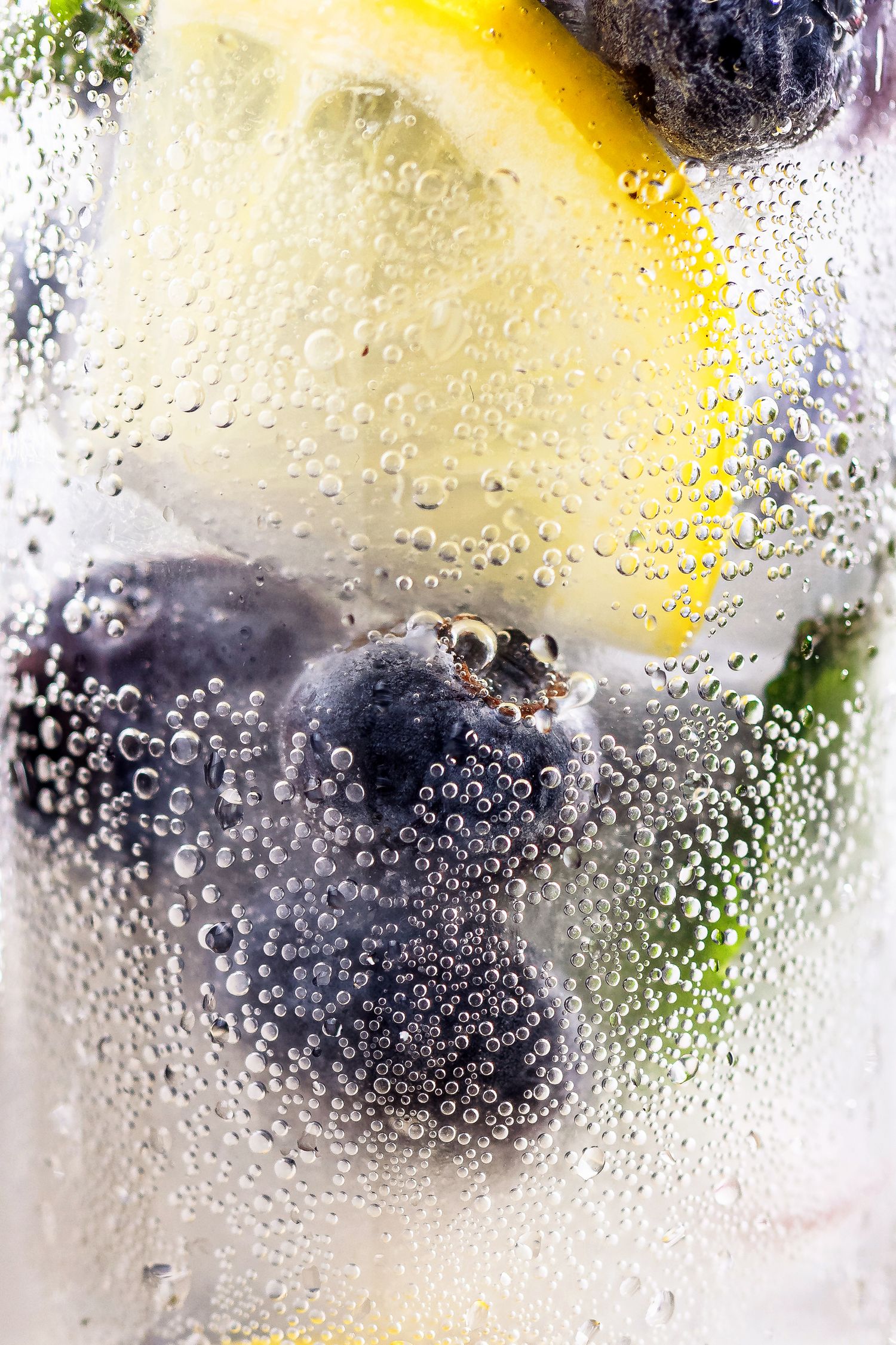 Close-up of sparkling water with blueberries and lemon slices, covered in condensation bubbles.
