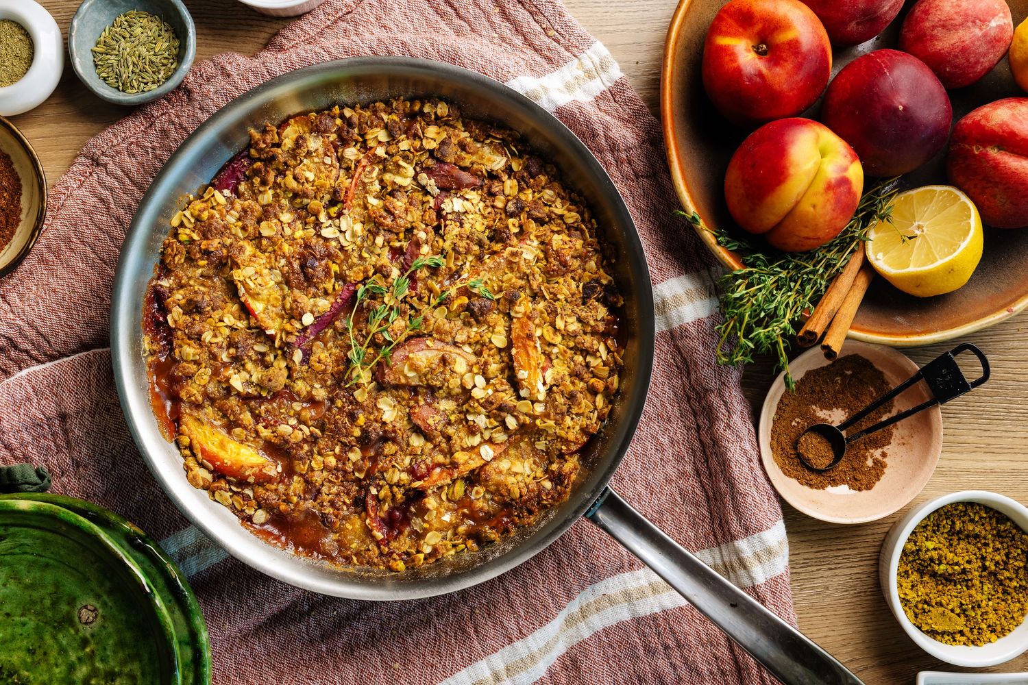 Savory skillet dish with grains, peaches, and herbs surrounded by fresh ingredients on a wooden table.
