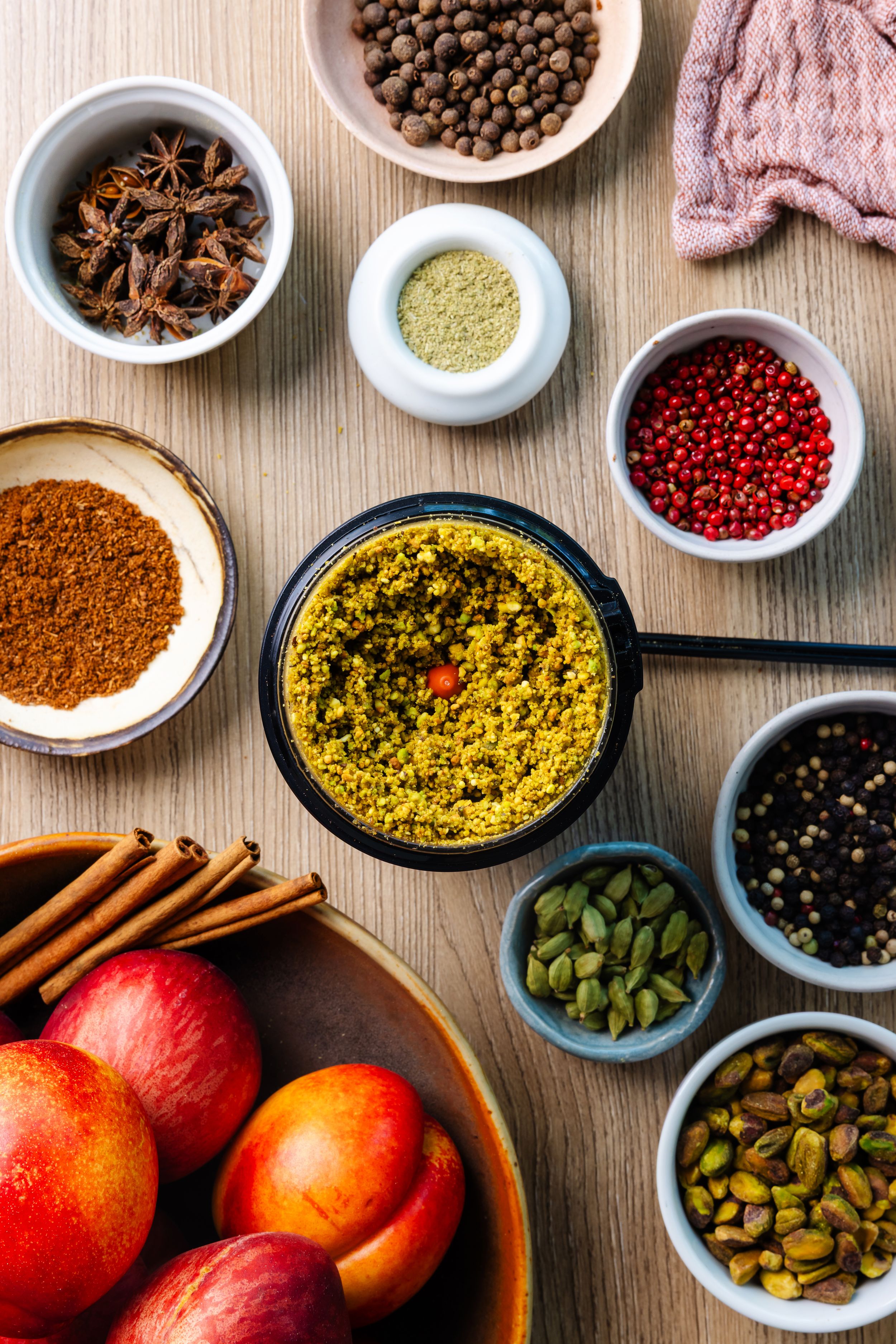 Assorted spices in a Krups grinder including star anise, cardamom, cinnamon, and peppercorns in bowls on wooden surface.