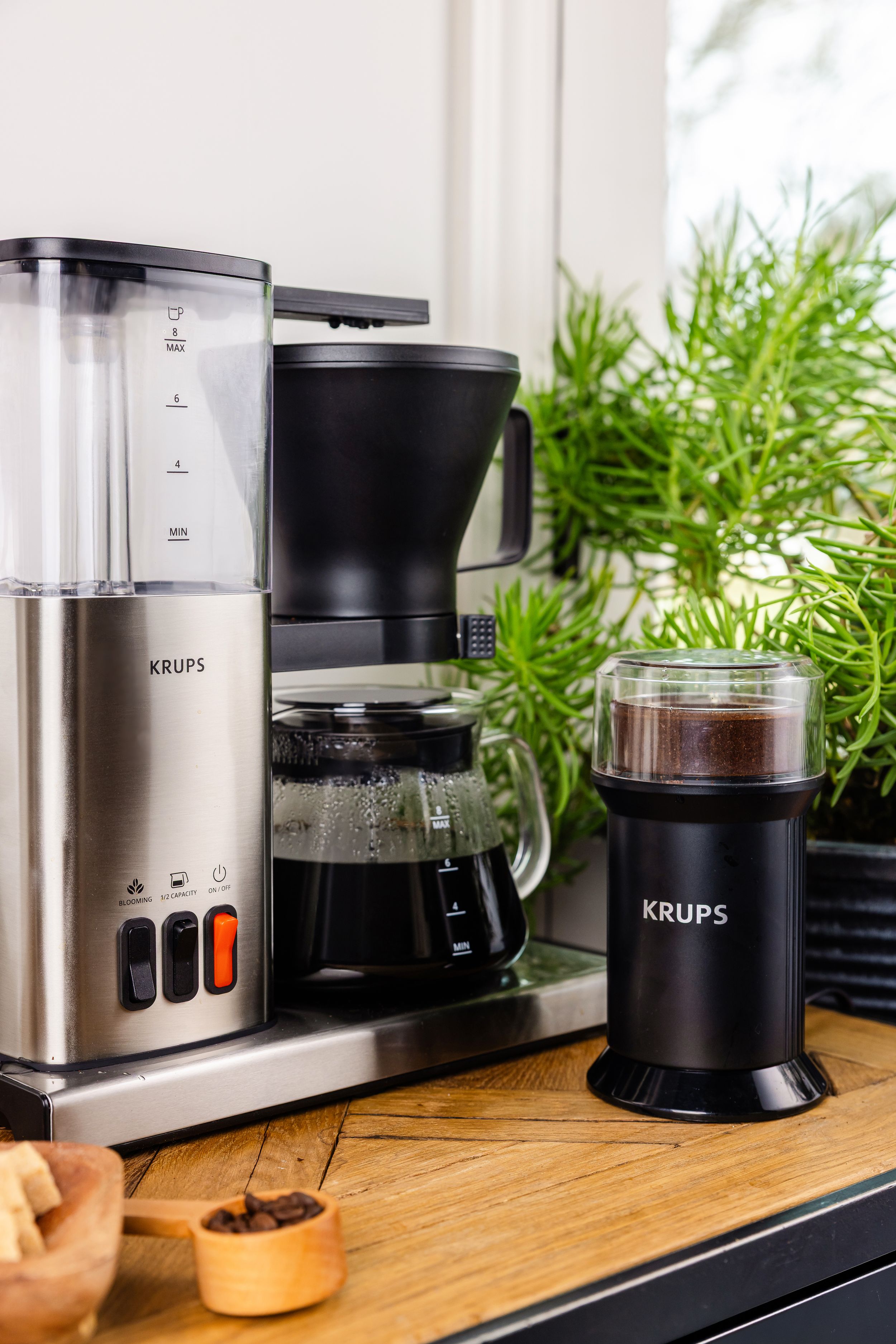 Krups stainless steel drip coffee maker with matching coffee grinder on wooden kitchen counter.