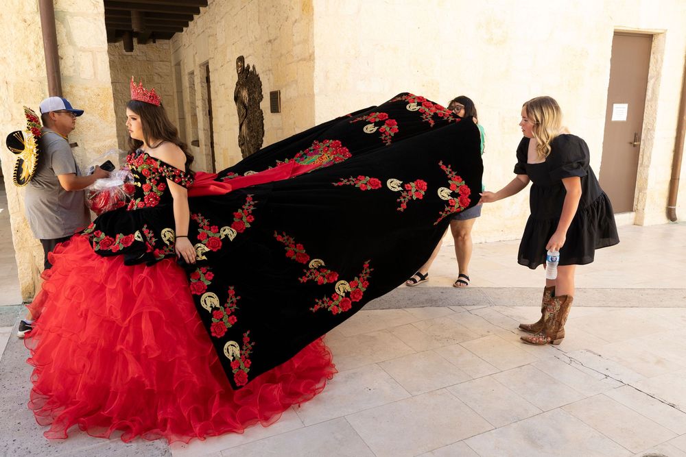 Dancers in black and red flamenco dresses perform in a line along a stone corridor.