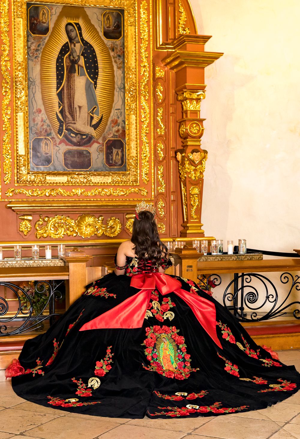 Ornate black and red Mexican dress with floral embroidery displayed against a golden religious altar backdrop.